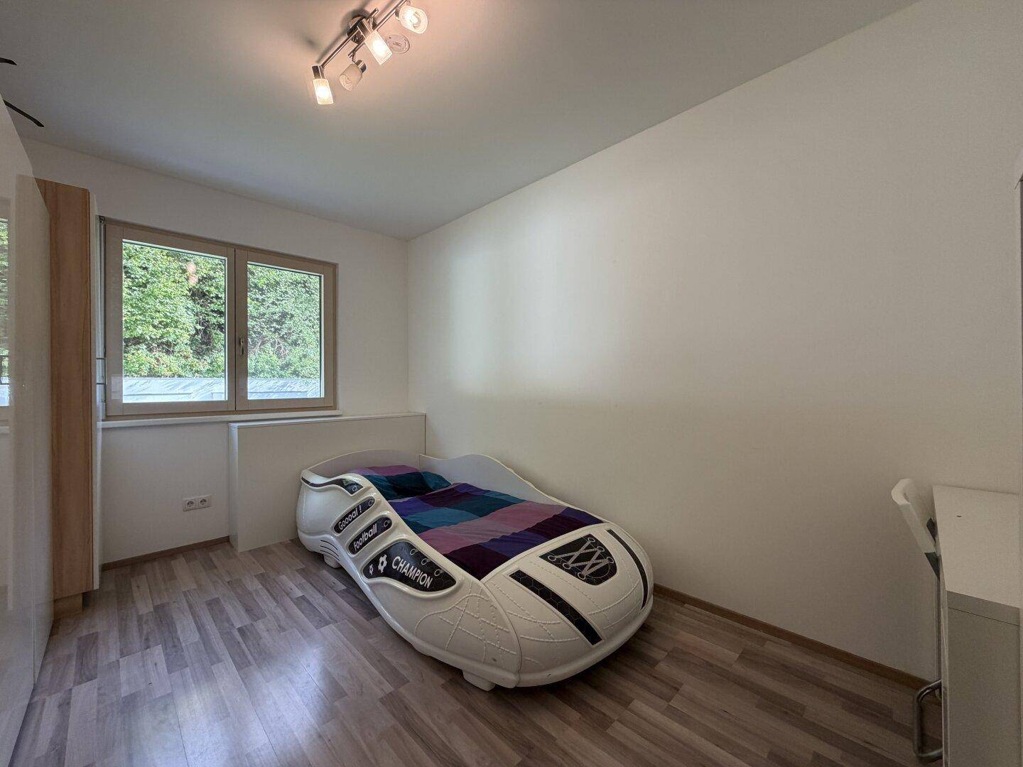 Kinderzimmer mit kreativem Autobett, Laminatboden und Fenster mit Blick ins Grüne.