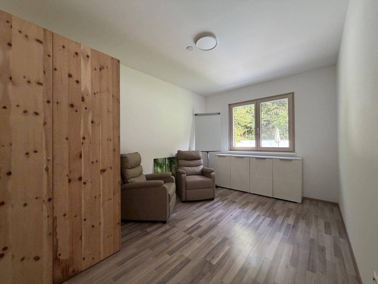 Helles Zimmer mit Holzschrank, bequemen Sesseln und Fenster mit Blick auf die Natur.