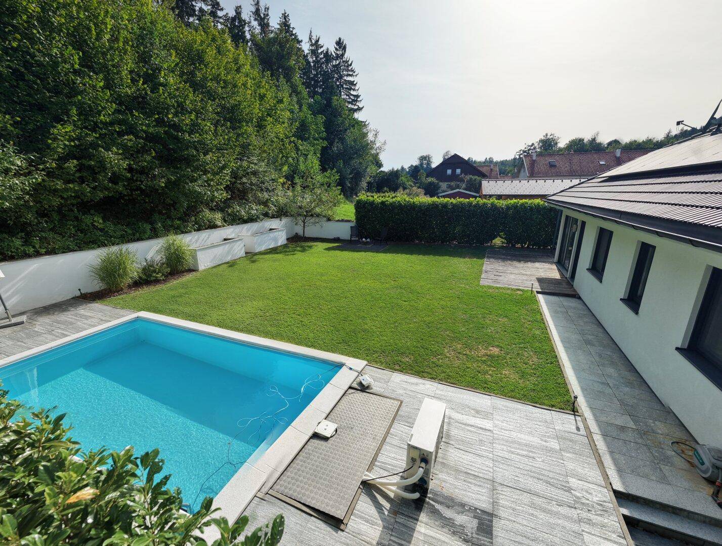 Außenbereich des Hauses mit Pool, gefliester Terrasse und Blick auf die umliegende Natur.
