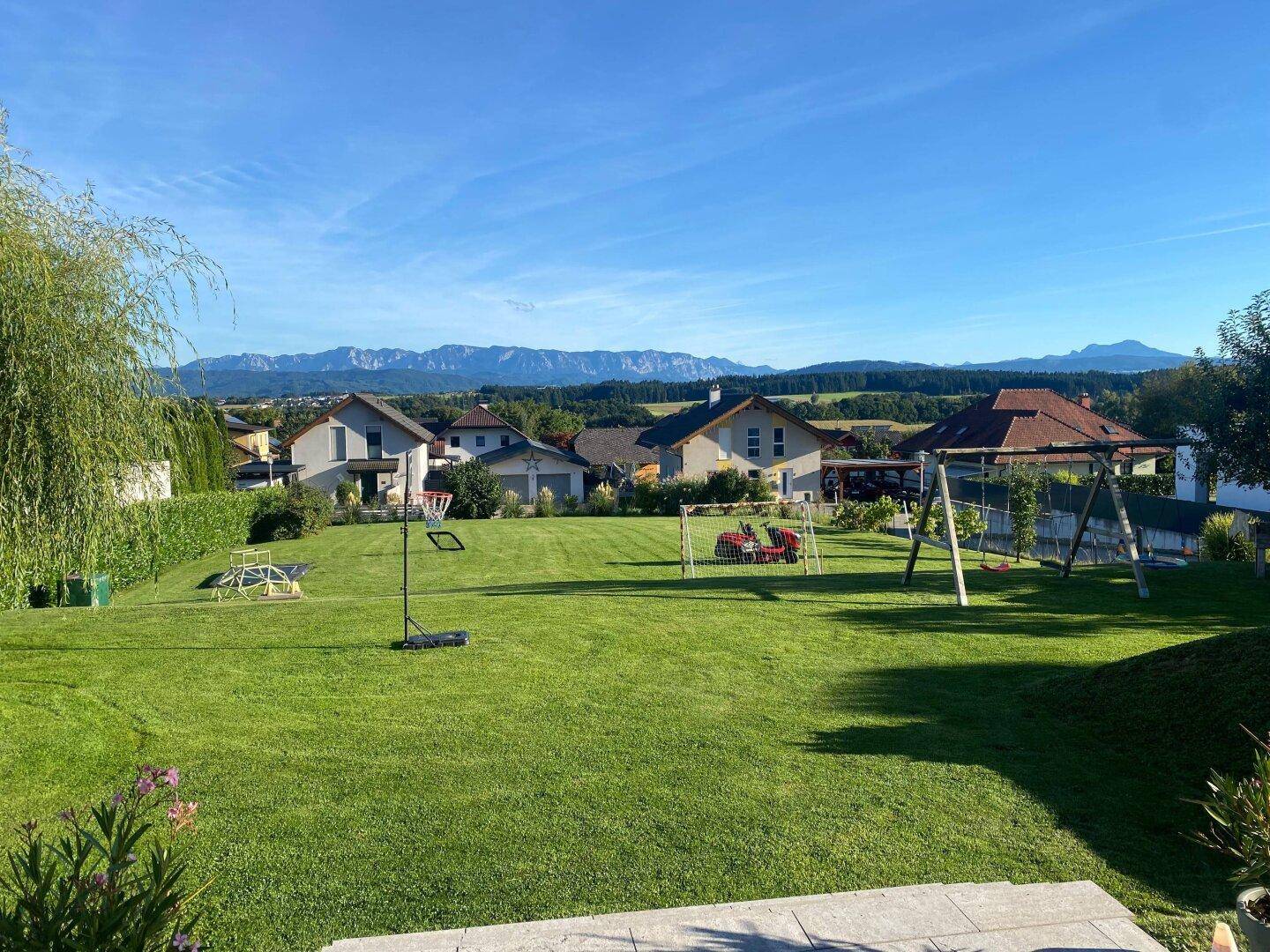 Großer Garten mit gepflegter Rasenfläche, Spielgeräten und weitem Blick auf die Berge.