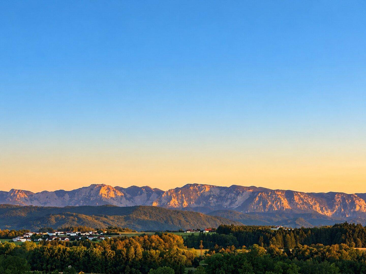 Panoramablick auf eine malerische Berglandschaft bei Sonnenuntergang mit einem Dorf im Vordergrund.