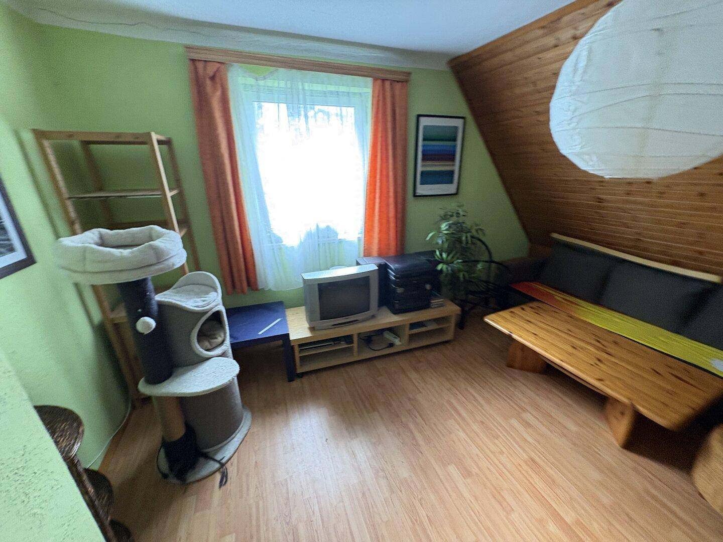 Gemütliches Wohnzimmer im Dachgeschoss mit Holzverkleidung, Schrägdecke und Laminatboden.