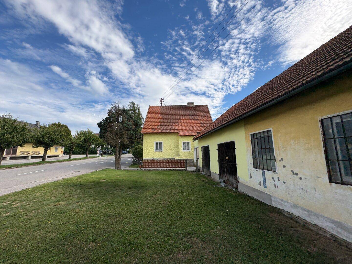 Gelbes Einfamilienhaus mit Nebengebäude und großem Rasenbereich unter blauem Himmel.