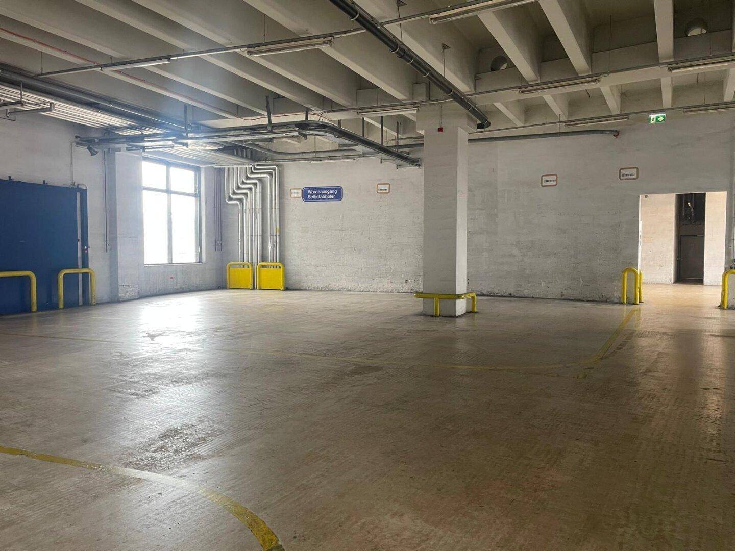 Geräumiger, leerer Gewerberaum mit Betonboden, Säulen und großen Fenstern für Tageslicht.