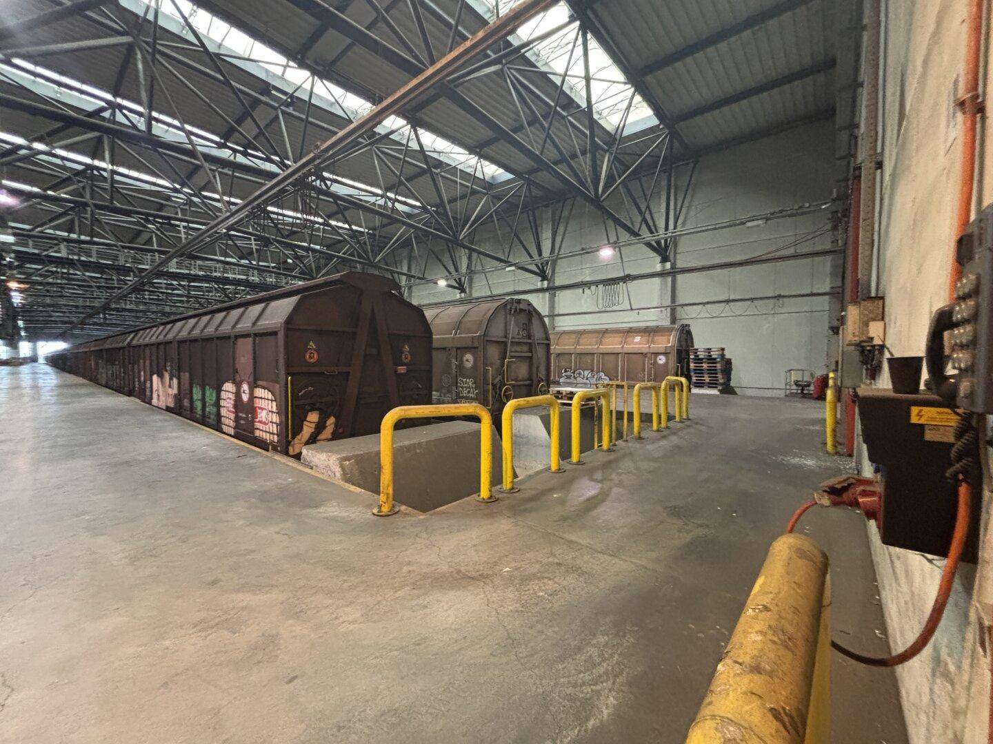 Große Lagerhalle mit hohen Decken, Oberlichtern und Gleisen für Güterwaggons.