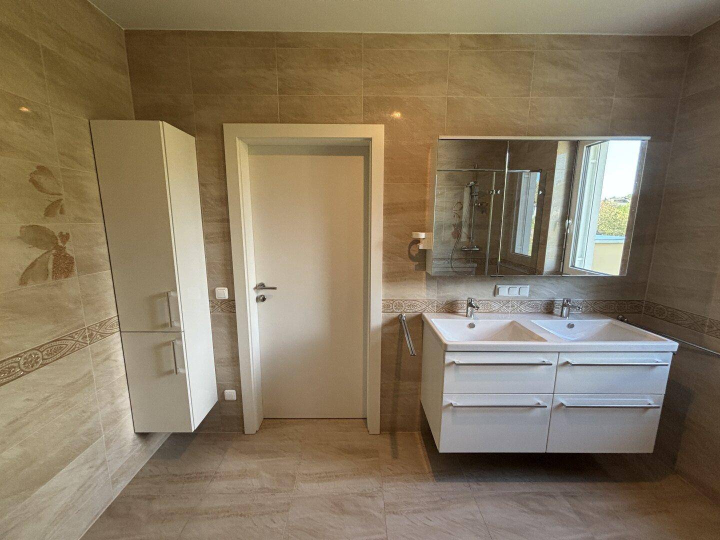 Modernes Badezimmer mit doppelten Waschbecken, Spiegelschrank und beigefarbenen Fliesen.