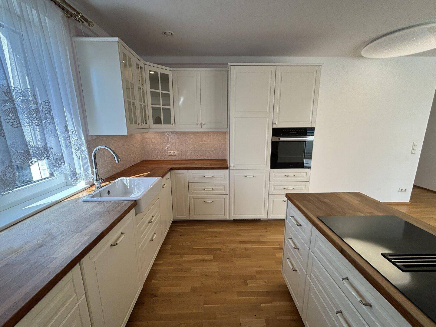 Moderne Küche mit weißen Schränken, Holz-Arbeitsplatten und hochwertigen Einbaugeräten.