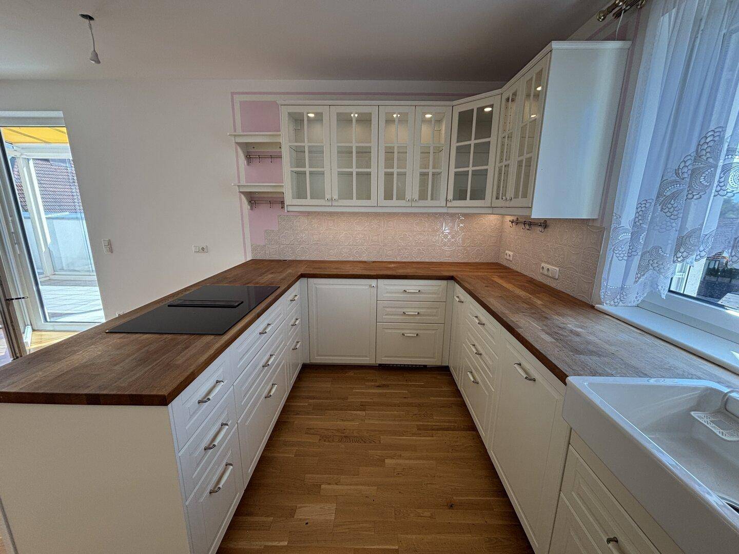 Helle Einbauküche mit weißen Schränken, Holz-Arbeitsplatten und integriertem Kochfeld.
