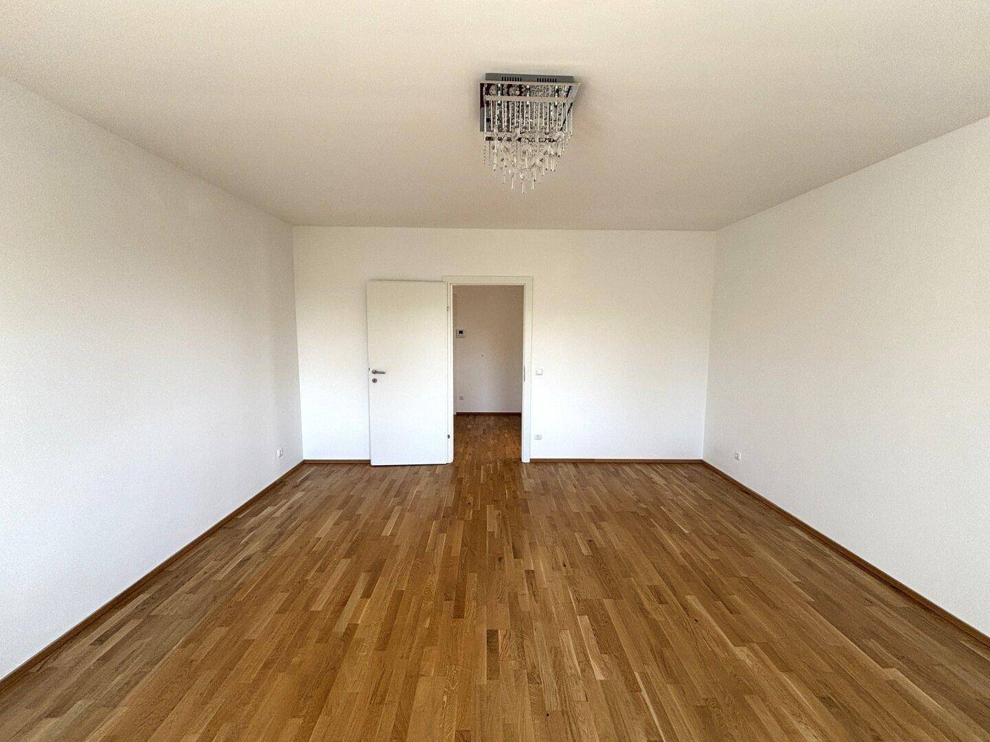 Geräumiges Zimmer mit Parkettboden und weiß gestrichenen Wänden, bietet viel Platz.