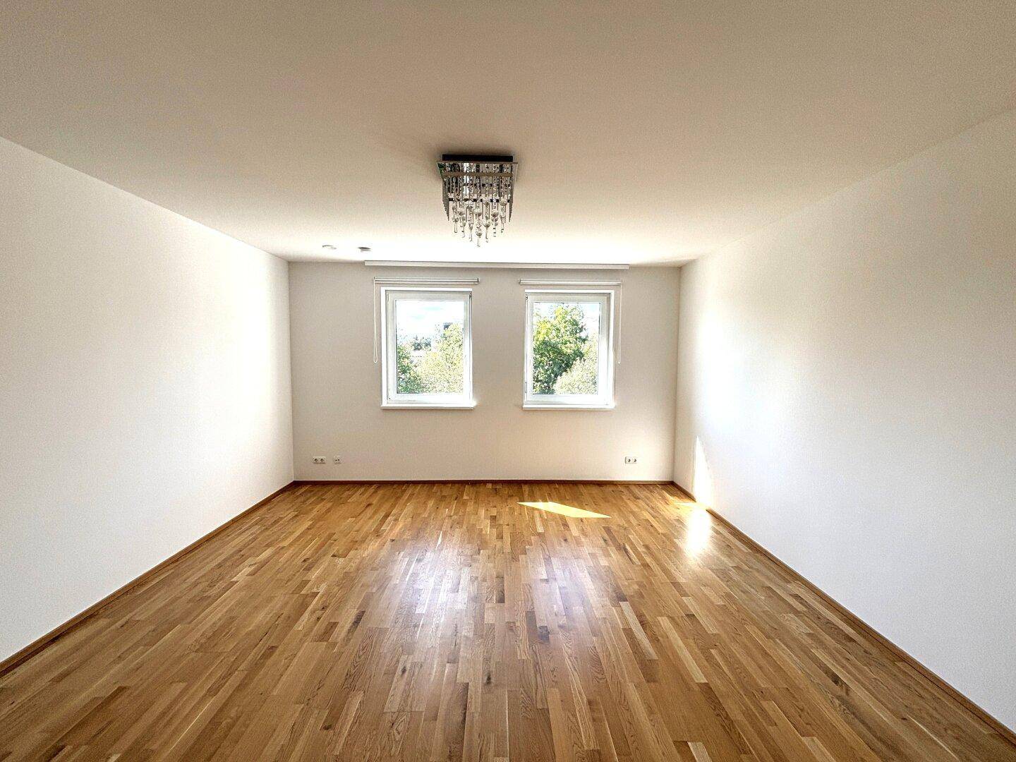 Helles Zimmer mit Holzparkettboden und zwei Fenstern, bereit zur individuellen Gestaltung.