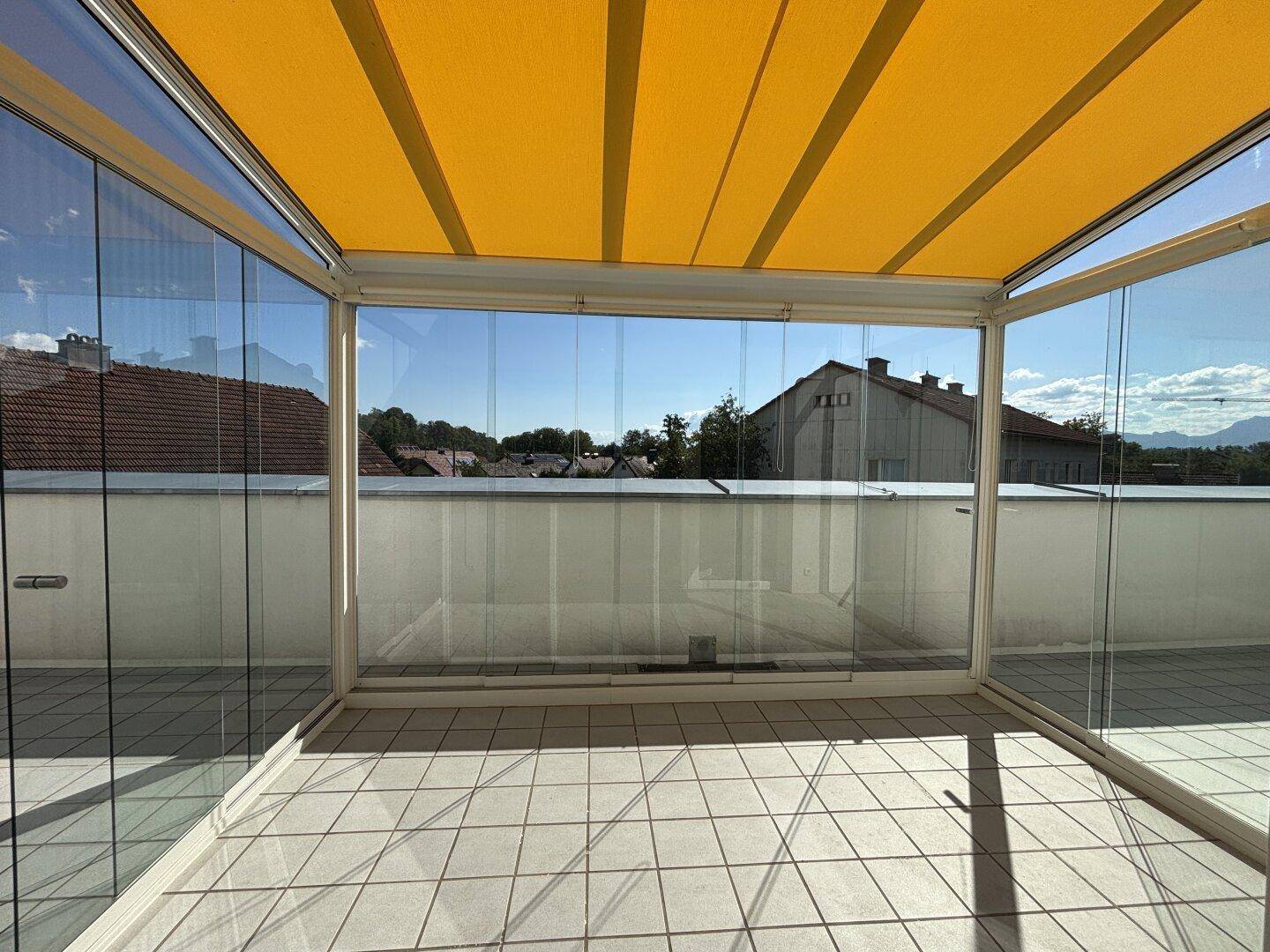 Verglaste Loggia mit Fliesenboden und gelbem Sonnenschutz, bietet weite Aussicht.