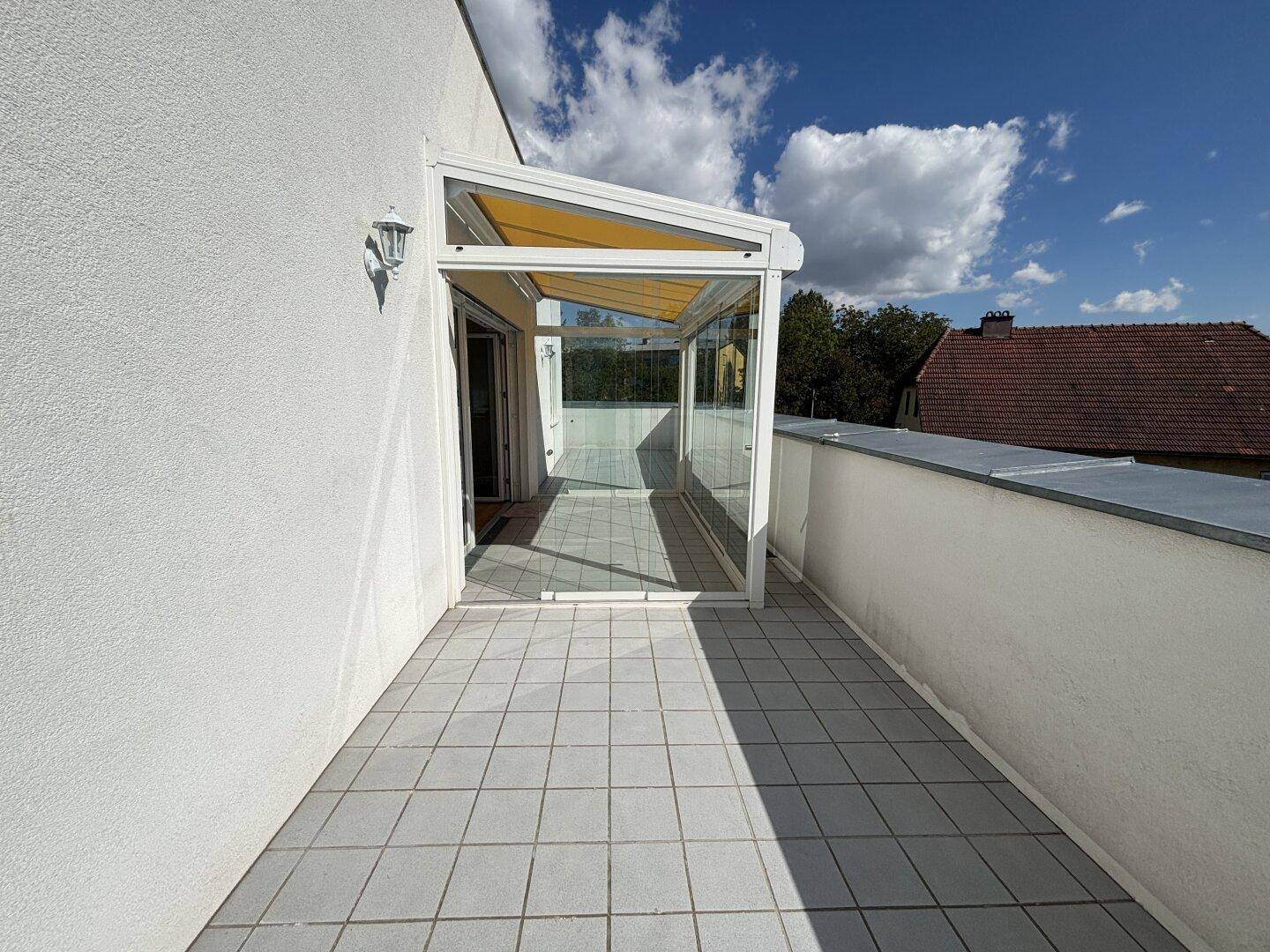 Sonniger Terrassenbereich mit Fliesen und einem verglasten Wintergarten, ideal zum Entspannen.