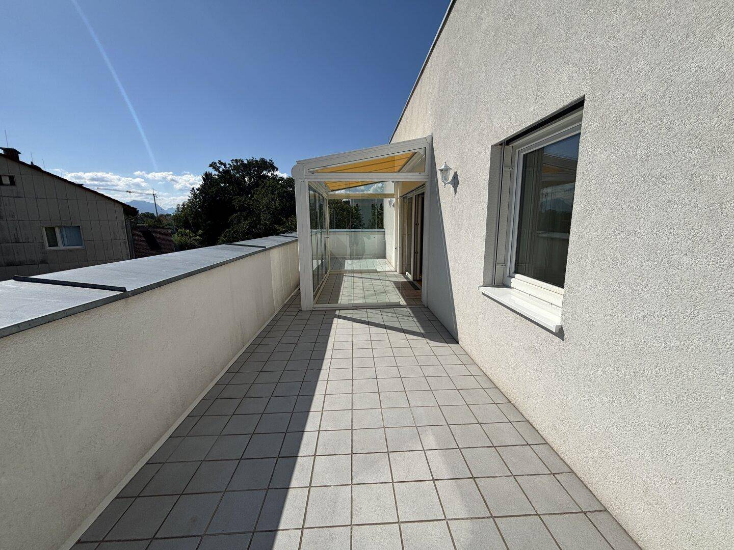 Große Dachterrasse mit Fliesenboden und integriertem Wintergarten unter blauem Himmel.