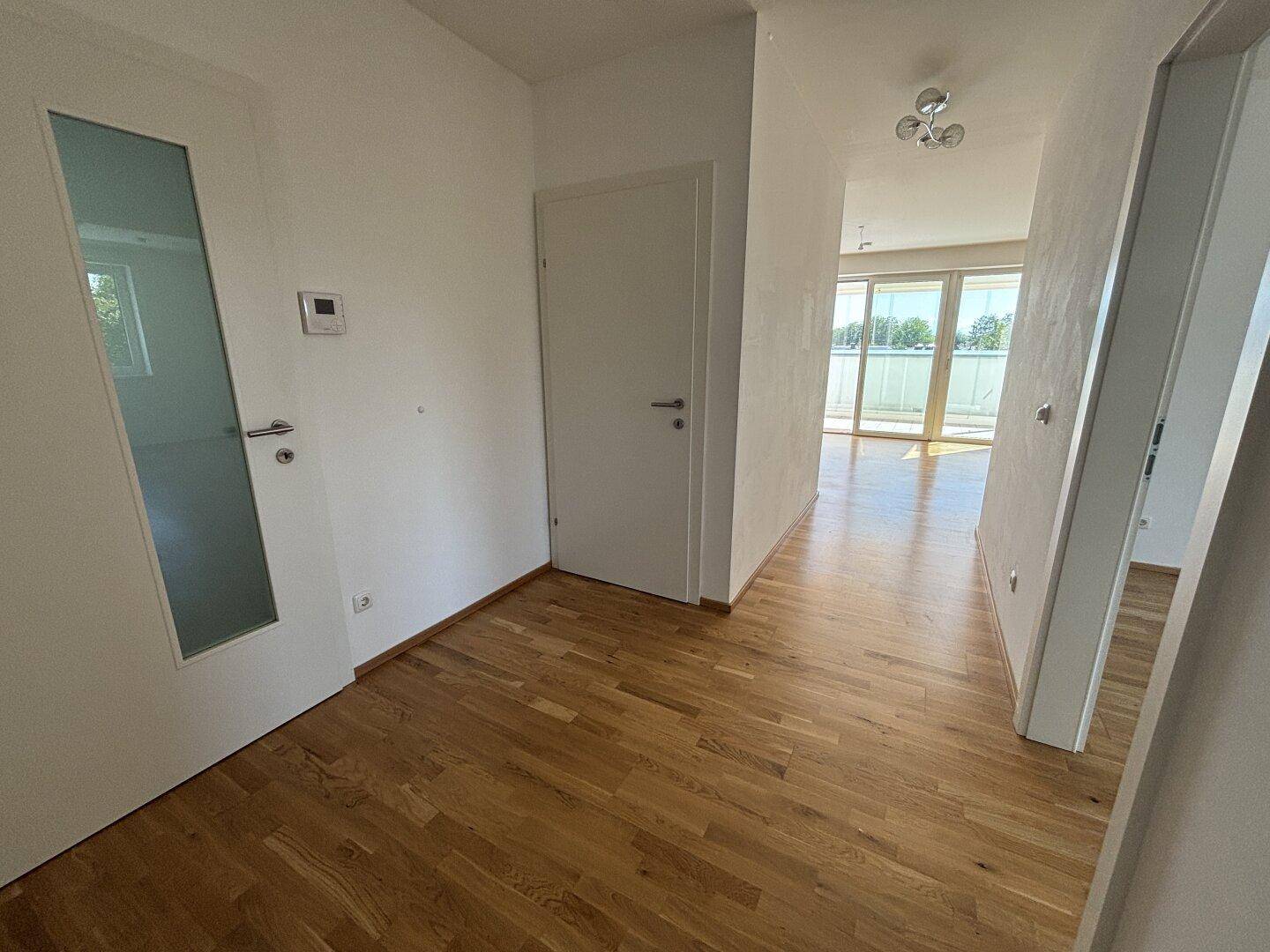 Heller Eingangsbereich mit Holzparkettboden, der in den offenen Wohnbereich führt.