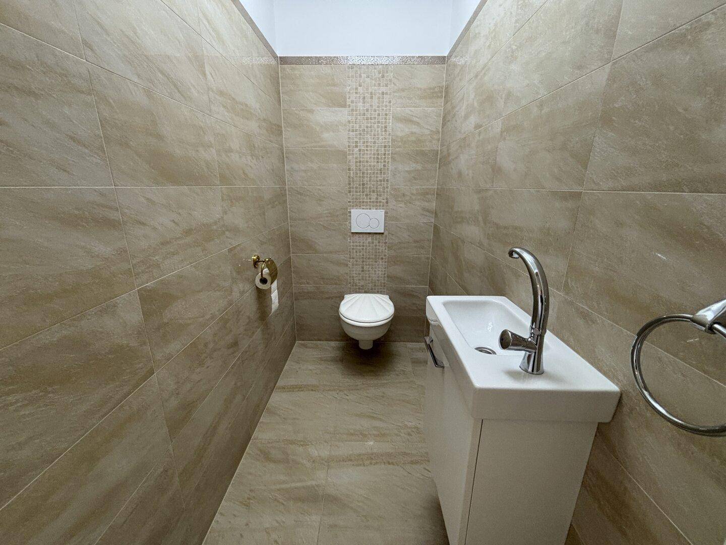 Kleines Gäste-WC mit Wand-WC und modernem Waschbecken, komplett gefliest.