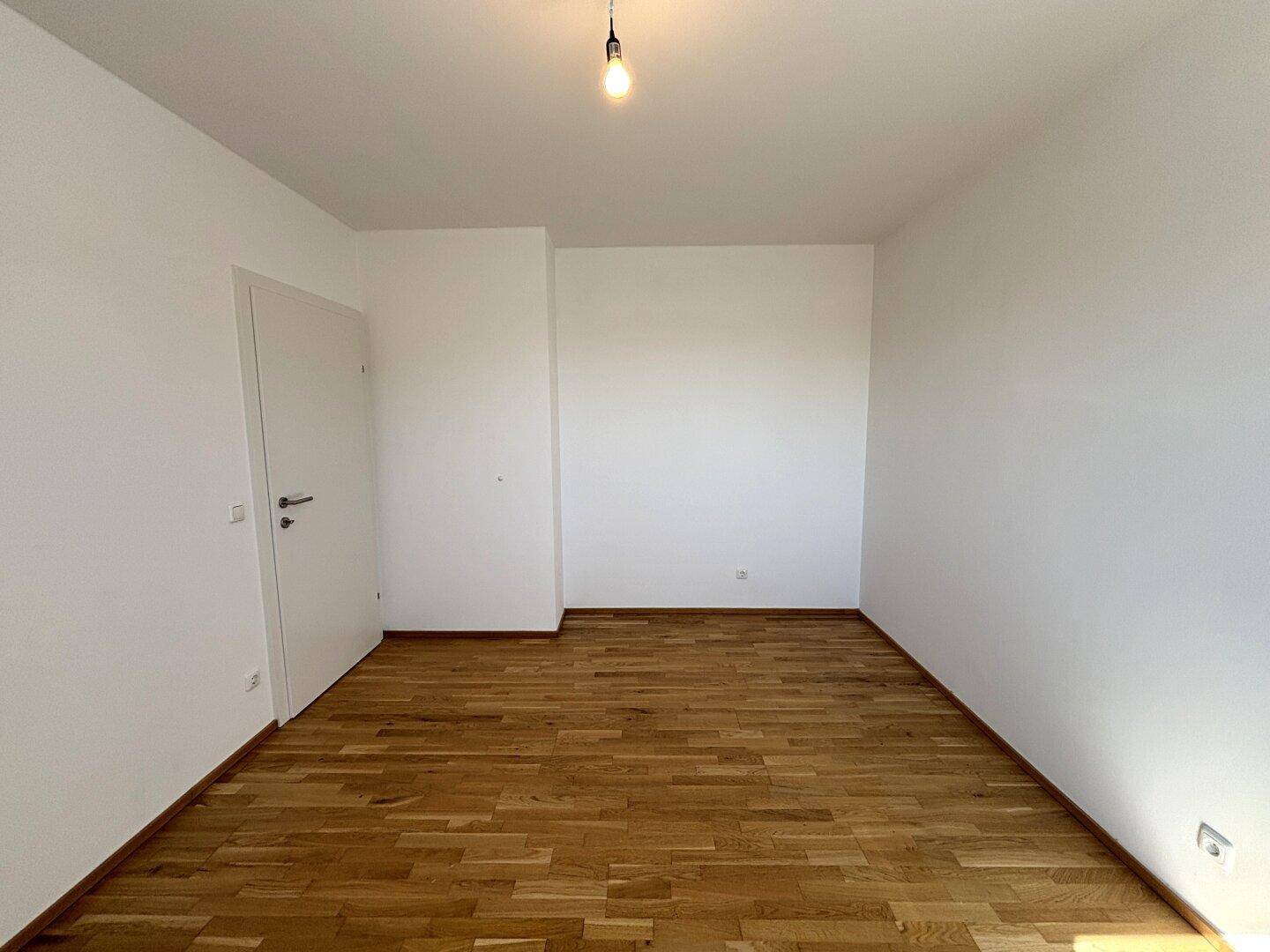 Leeres Zimmer mit Holzparkettboden und weiß gestrichenen Wänden, vielseitig nutzbar.