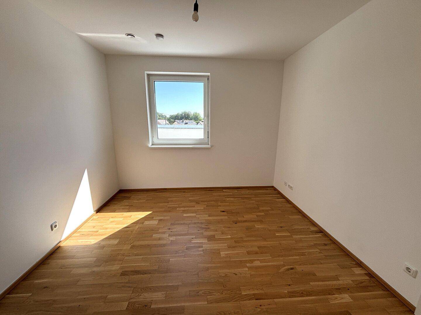 Sonniger Raum mit Parkettboden und einem Fenster, das viel Tageslicht spendet.