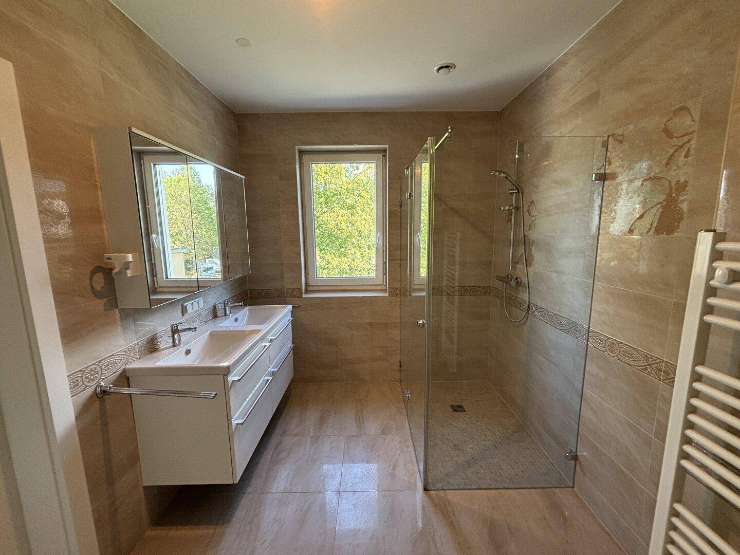 Geräumiges Badezimmer mit begehbarer Dusche, Doppelwaschbecken und Fenster.