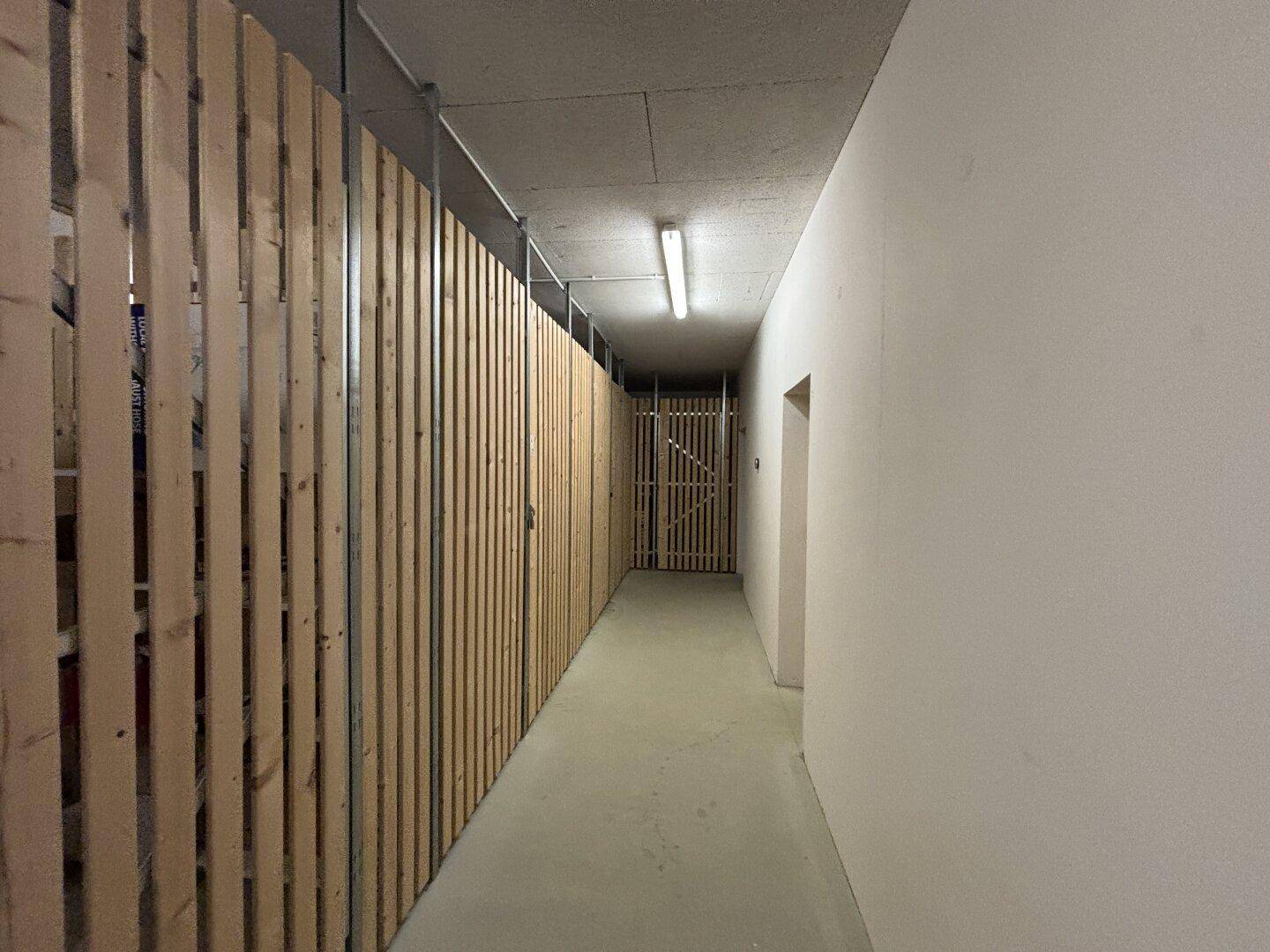 Kellerabteil mit Holzabtrennungen und Betonboden, bietet zusätzlichen Stauraum.