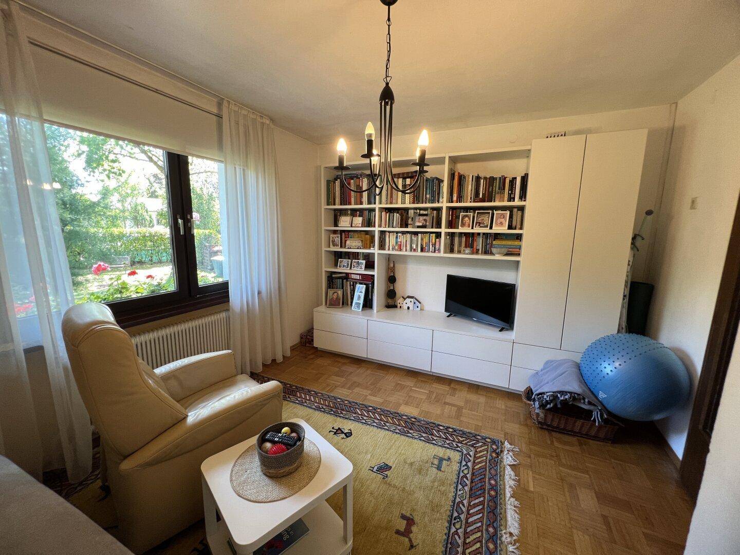 Helles Wohnzimmer mit großem Wandregal, Fernseher und bequemen Sitzgelegenheiten.