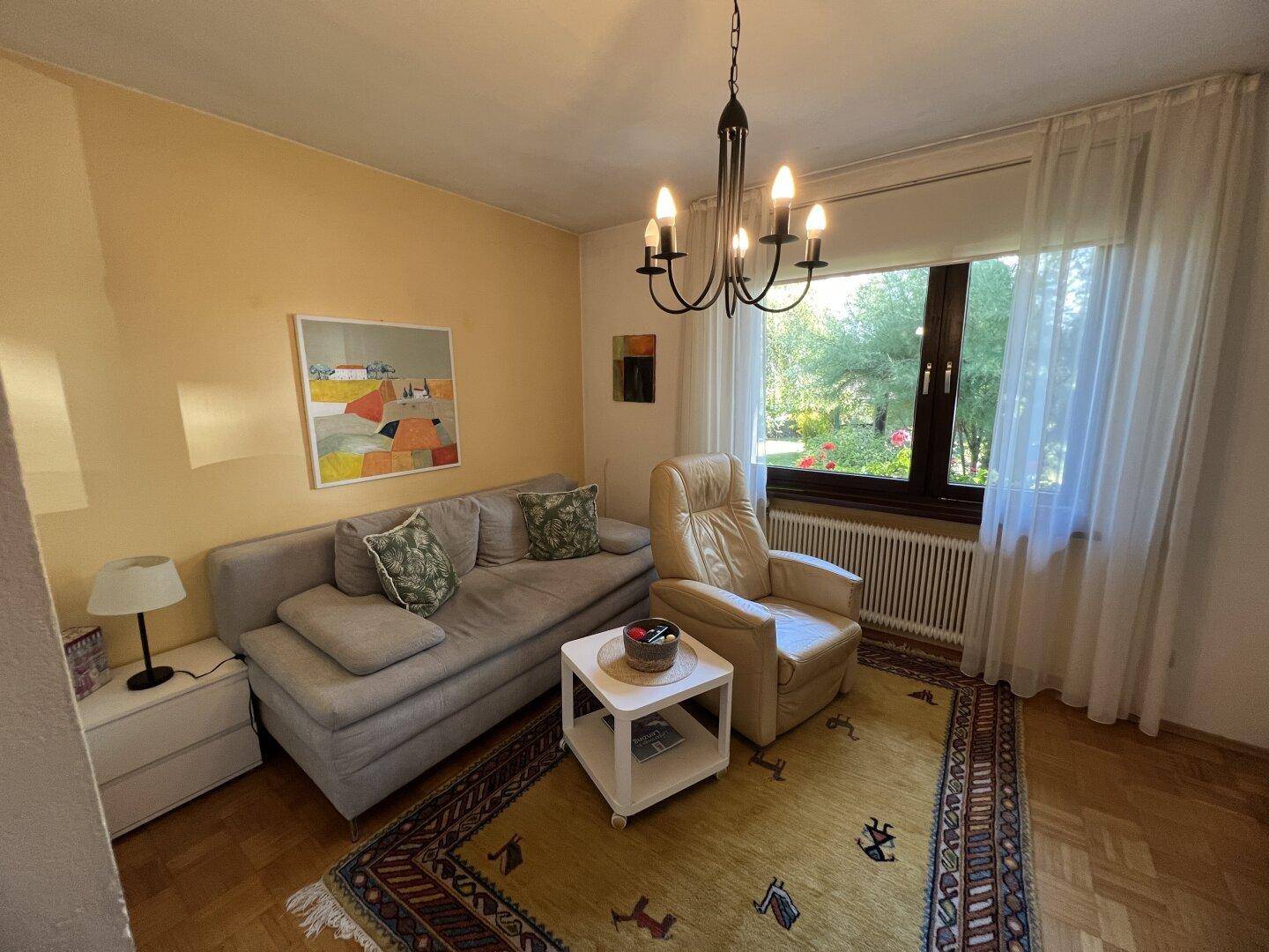 Gemütliches Wohnzimmer mit Sofa und Sessel, bietet einen schönen Blick ins Grüne.