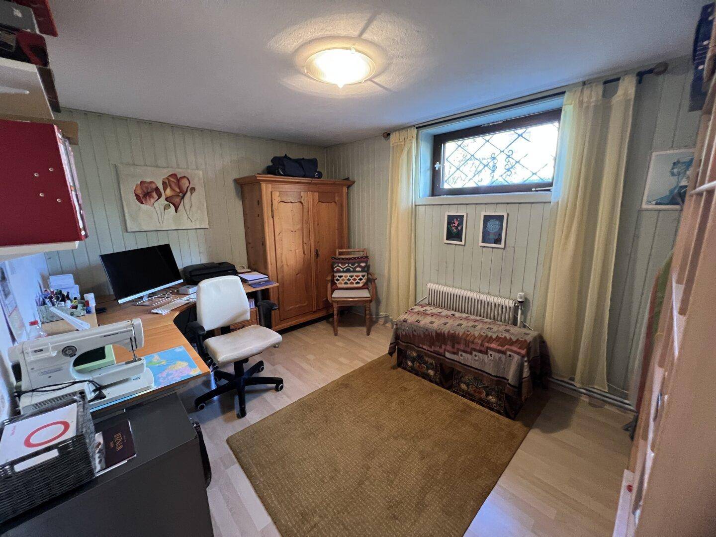 Funktional eingerichtetes Zimmer mit Schreibtisch, Kleiderschrank und Teppich, nutzbar als Arbeits- oder Gästezimmer.