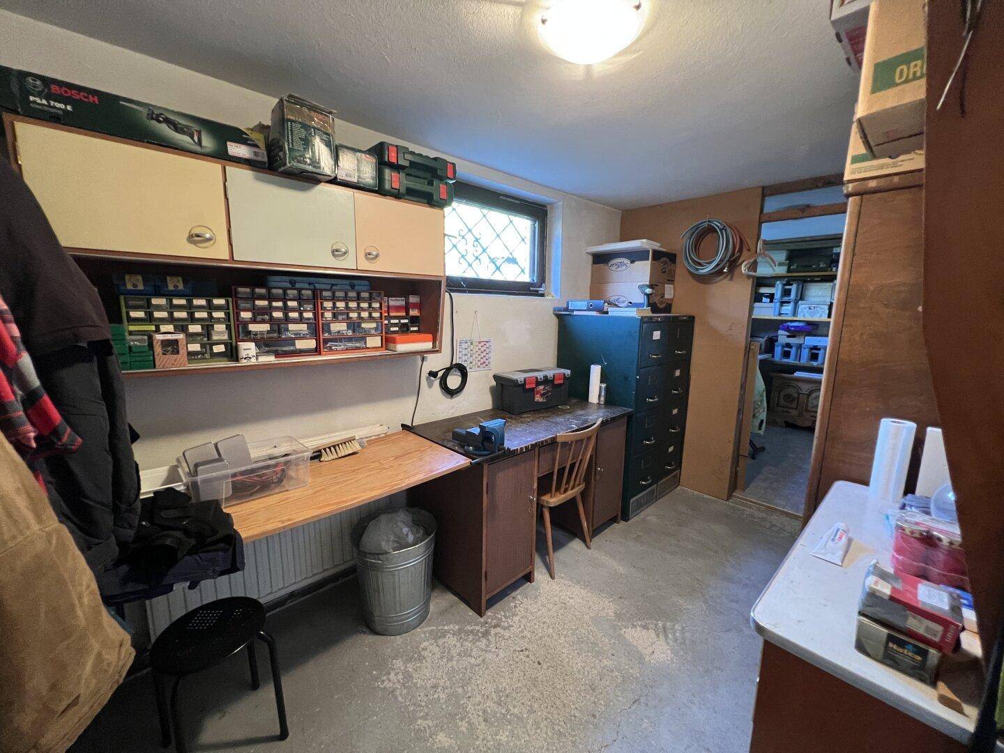Praktischer Werkstattraum im Keller mit Werkbank, Schränken und Betonboden für handwerkliche Tätigkeiten.
