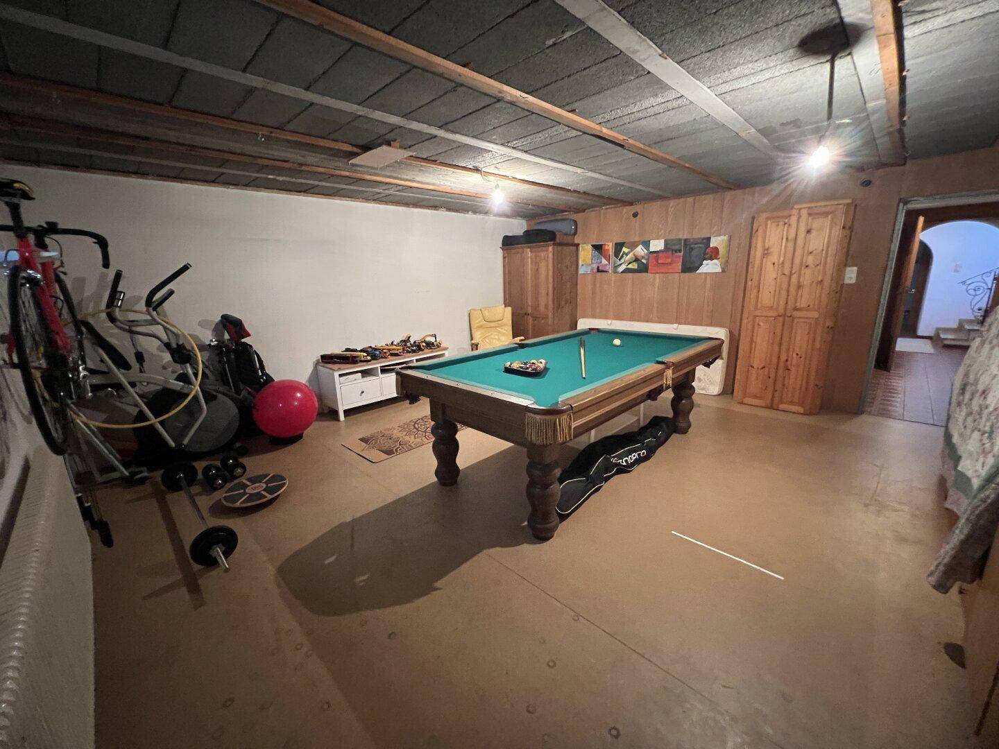Geräumiger Kellerraum mit Billardtisch und Fitnessgeräten, perfekt für Freizeit und Sport.