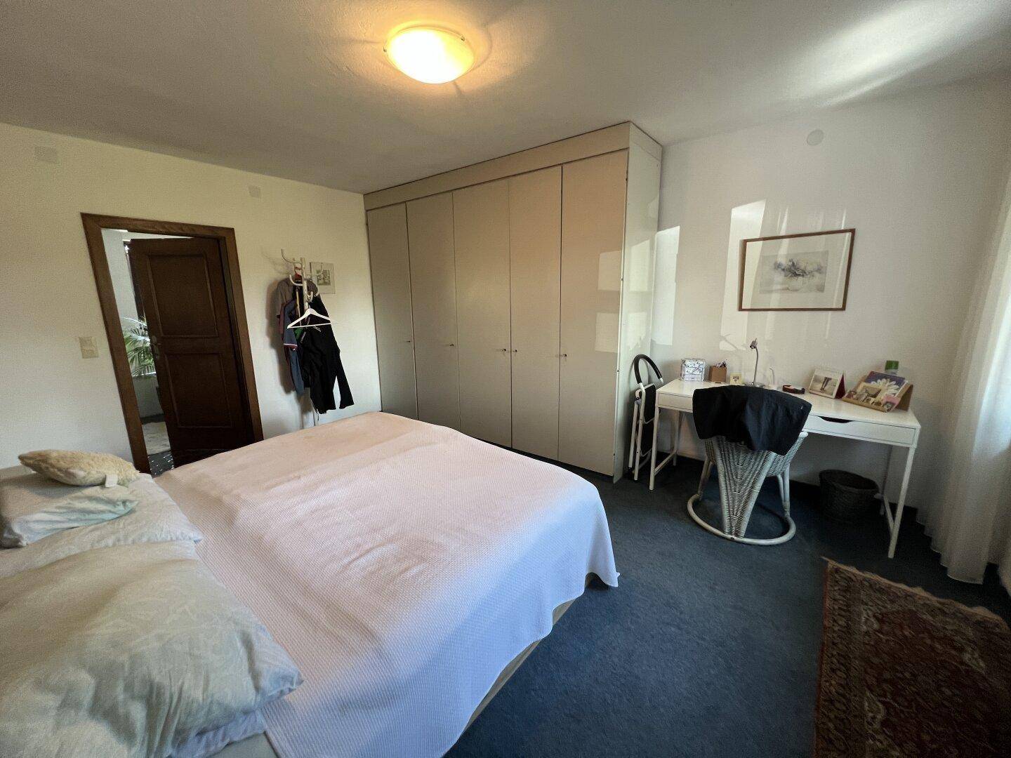 Schlafzimmer mit praktischen Einbauschränken und einem Schreibtisch am Fenster.