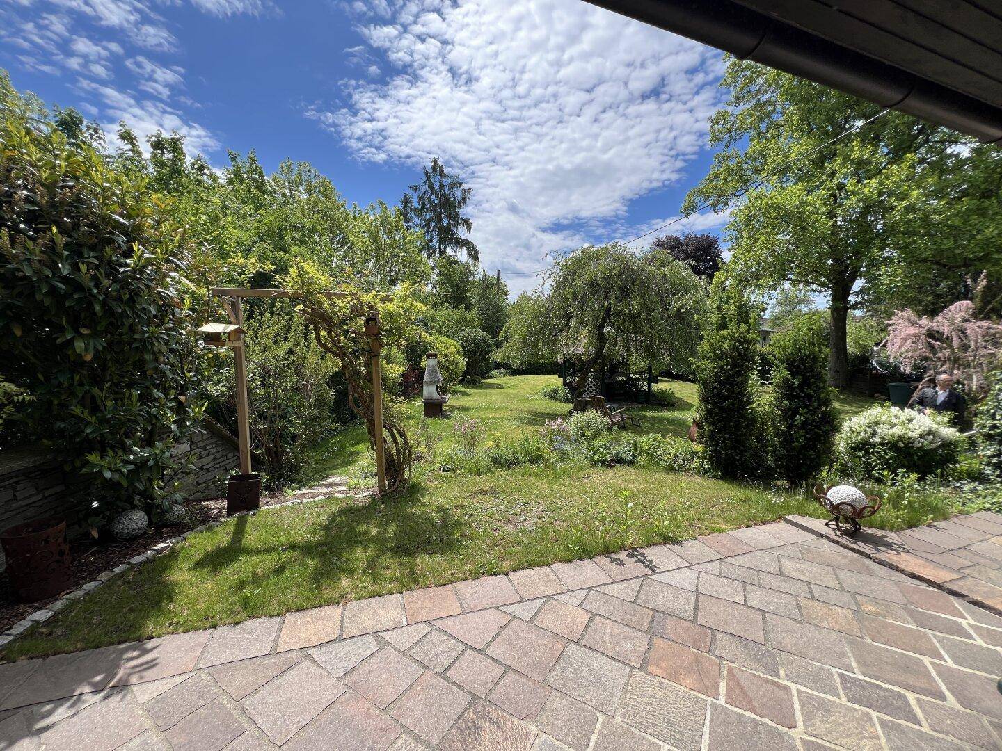 Weitläufiger, grüner Garten mit altem Baumbestand, gesehen von der Terrasse.