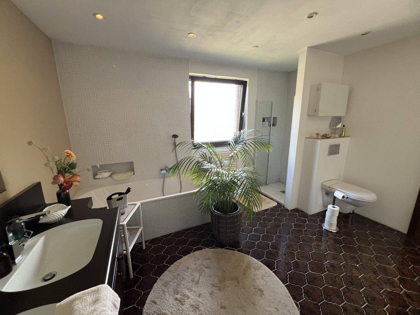 Modernes Badezimmer mit Badewanne, Duschbereich und wandhängendem WC.