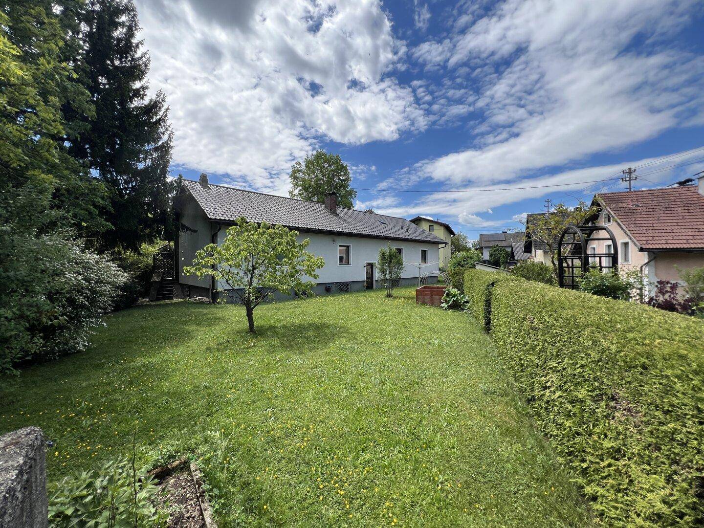 Großzügiger Garten mit gepflegtem Rasen, Hecke und einem freistehenden Haus unter blauem Himmel.