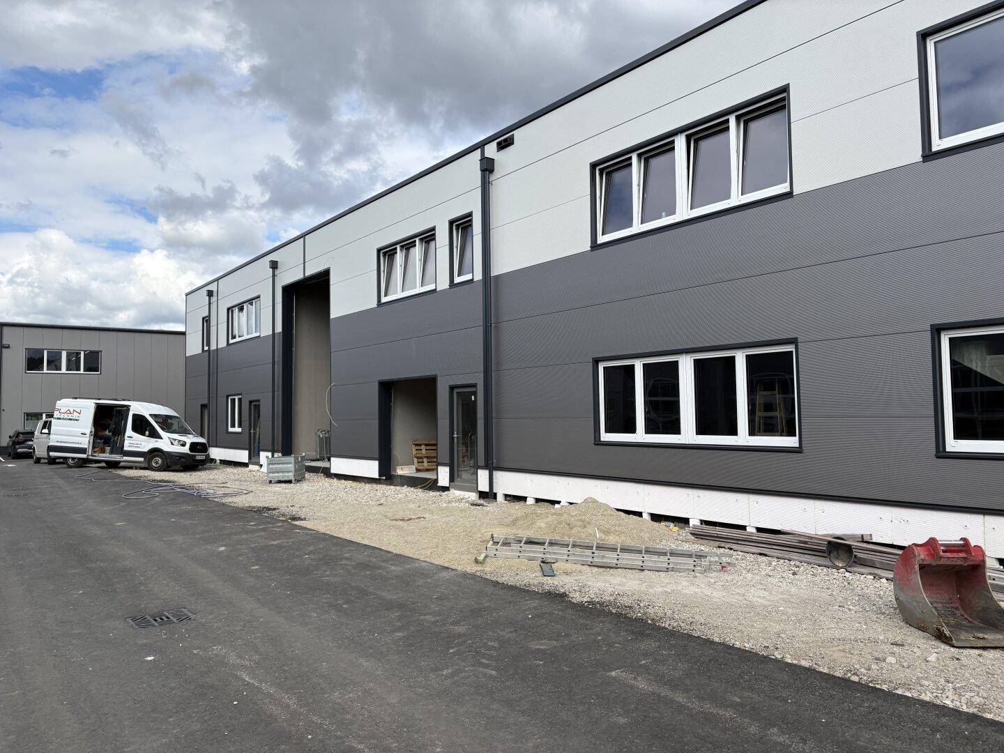 Seitenansicht eines neuen Geschäftsgebäudes mit zweifarbiger Fassade und Baustellenbereich im Vordergrund.