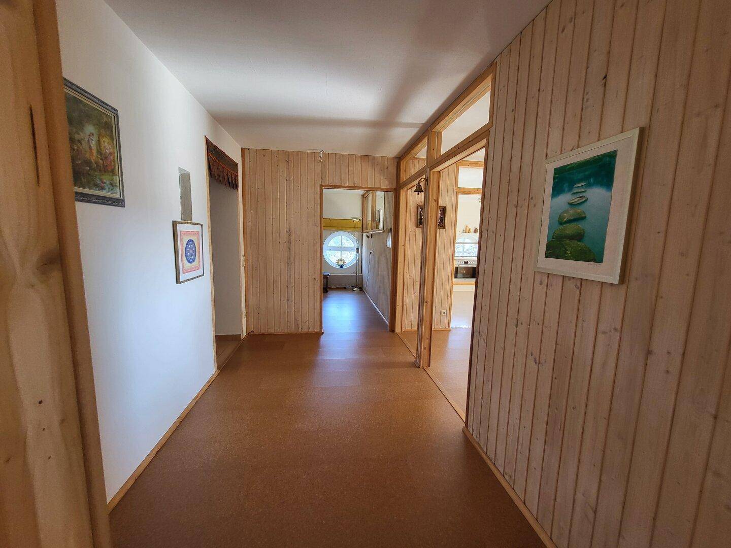 Flur mit Holzvertäfelung an den Wänden und einem hellbraunen Boden, der zu weiteren Räumen führt.