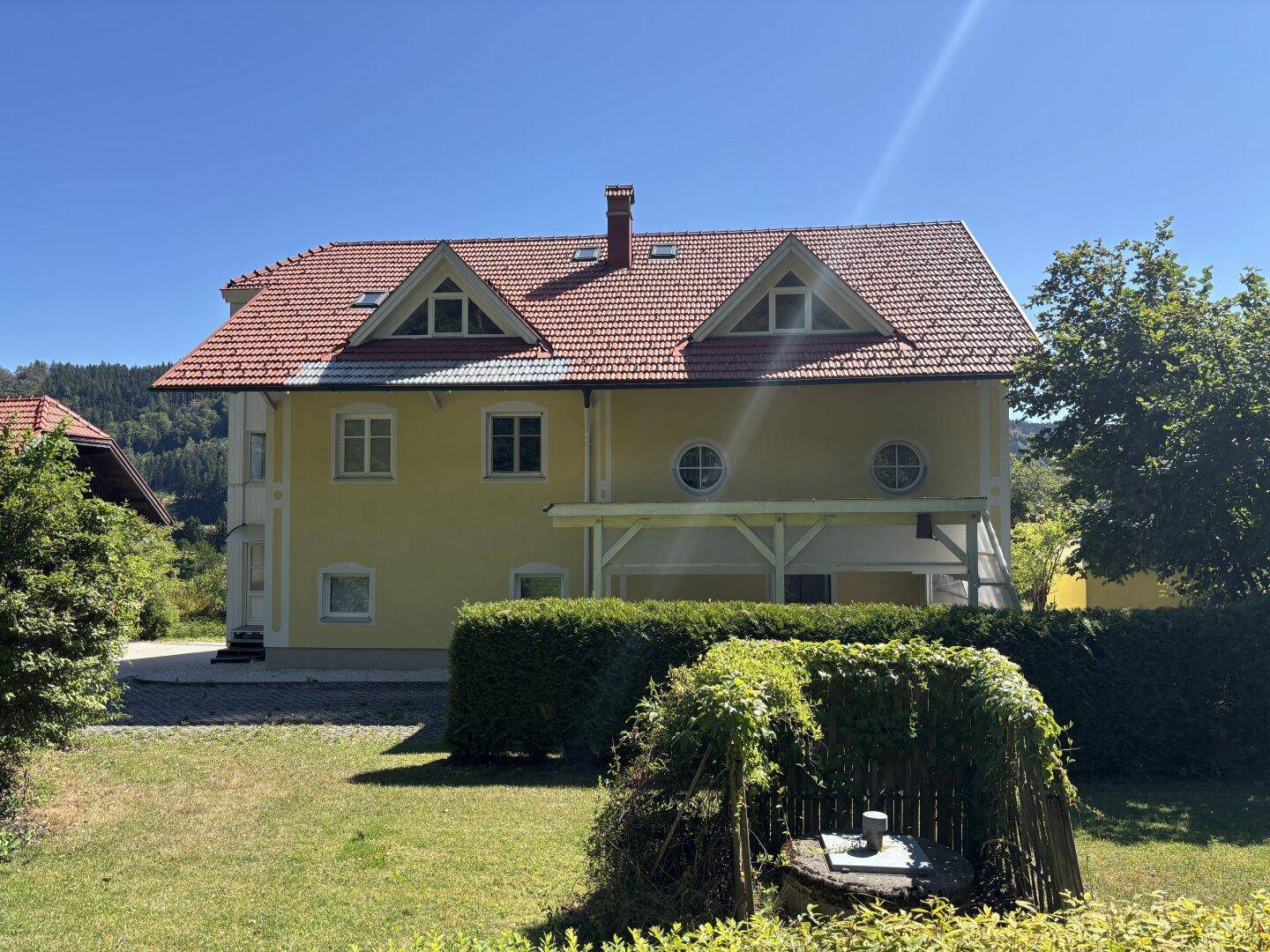 Vorderansicht des Hauses vom Garten aus mit überdachtem Terrassenbereich und einem Brunnen.