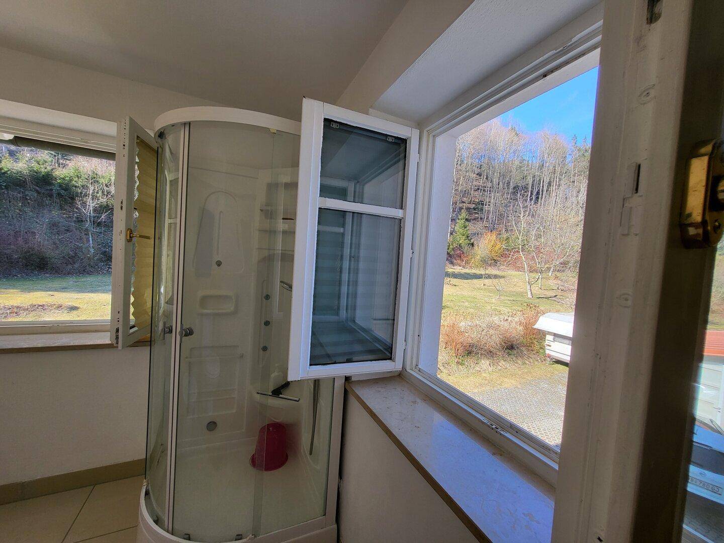 Badezimmer mit Duschkabine und Fenster mit Blick ins Grüne.