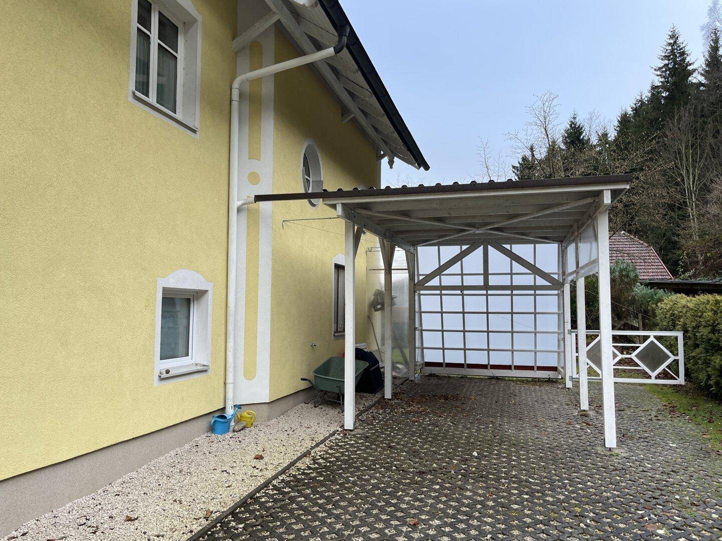 Überdachter Carport neben dem Haus mit gelber Fassade.