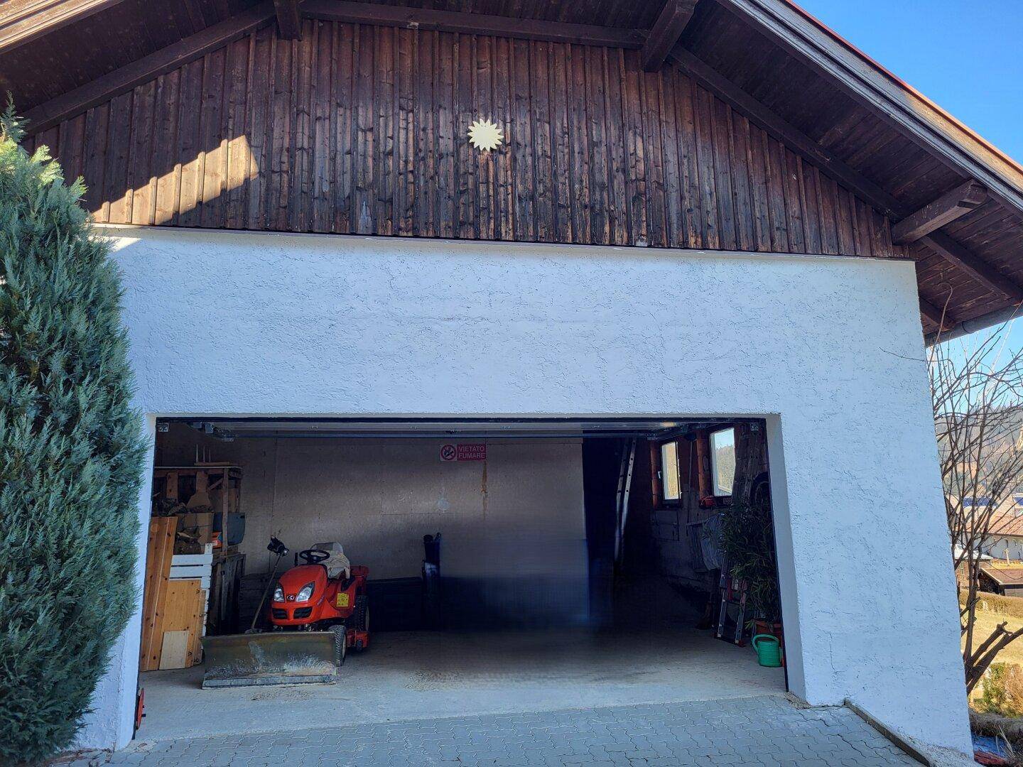 Offene Garage mit Stauraum und einem kleinen Rasenmäher.