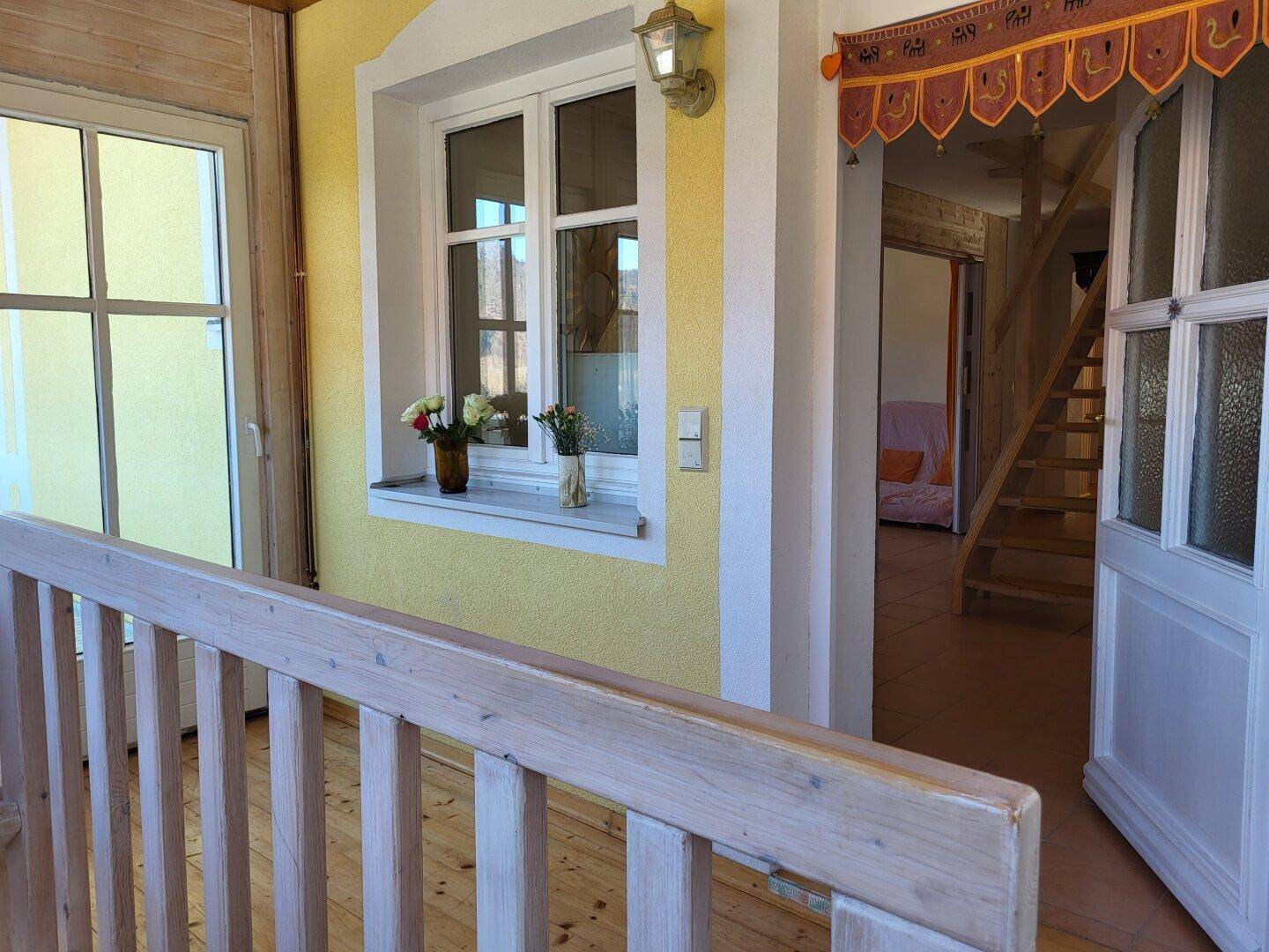 Flur oder Treppenabsatz mit Holzgeländer, Fenstern und Blick in einen weiteren Raum mit Treppe.