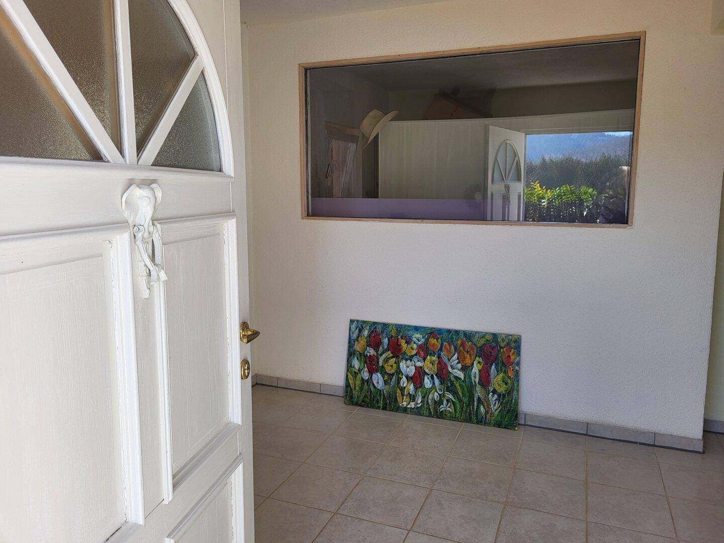 Eingangsbereich mit Fliesenboden, einer weißen Tür und einem farbenfrohen Gemälde an der Wand.