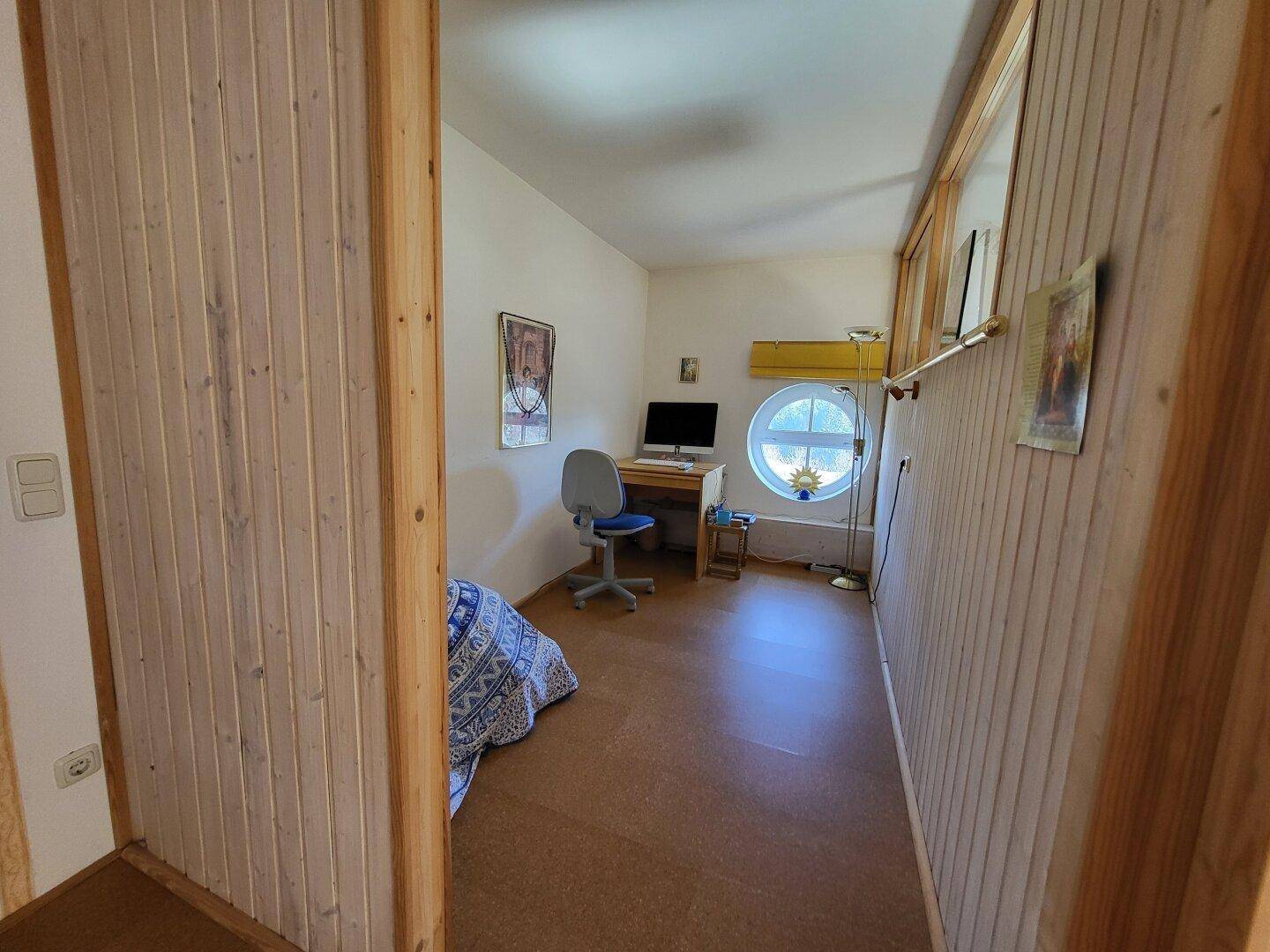 Kleiner Raum, möglicherweise ein Büro oder Gästezimmer, mit Schreibtisch, Stuhl und einem runden Fenster.