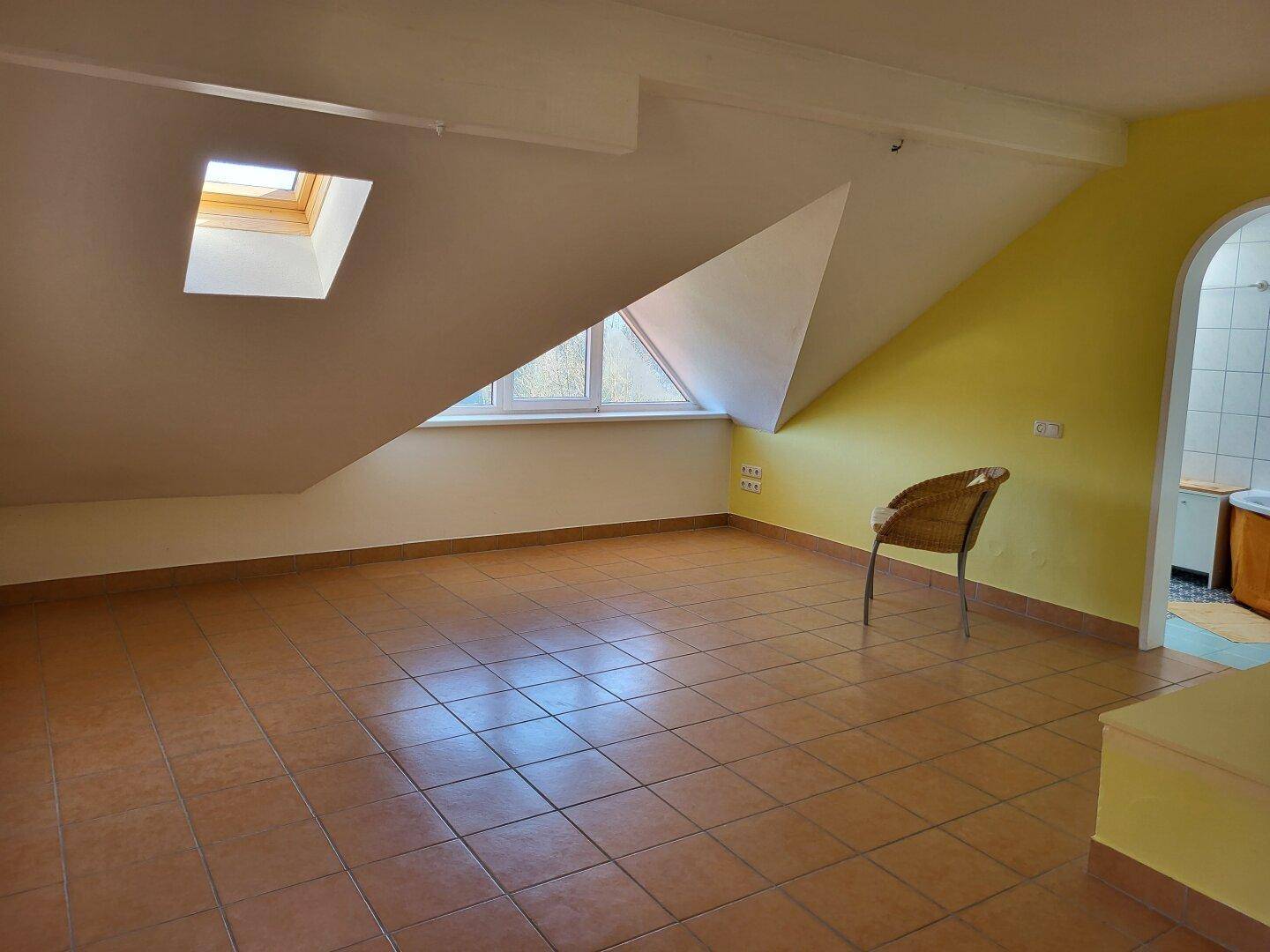 Helles Dachzimmer mit Fliesenboden, Dachschrägen und einem kleinen Fenster.