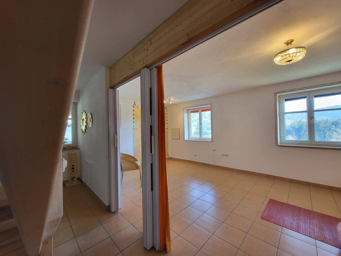 Raum mit Fliesenboden, einer Falttür und Fenstern, die viel Tageslicht hereinlassen.