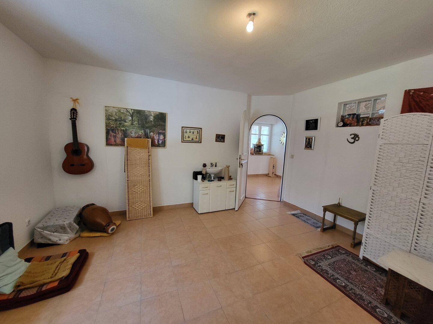 Geräumiger Wohnbereich mit hellen Fliesen, Gitarre und spirituellen Dekorationen.