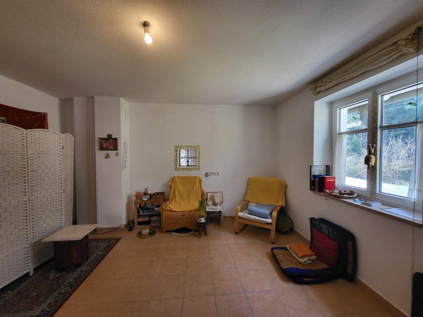 Wohnzimmer mit Fliesenboden, einem weißen Paravent und zwei gelben Sesseln, hell und gemütlich.