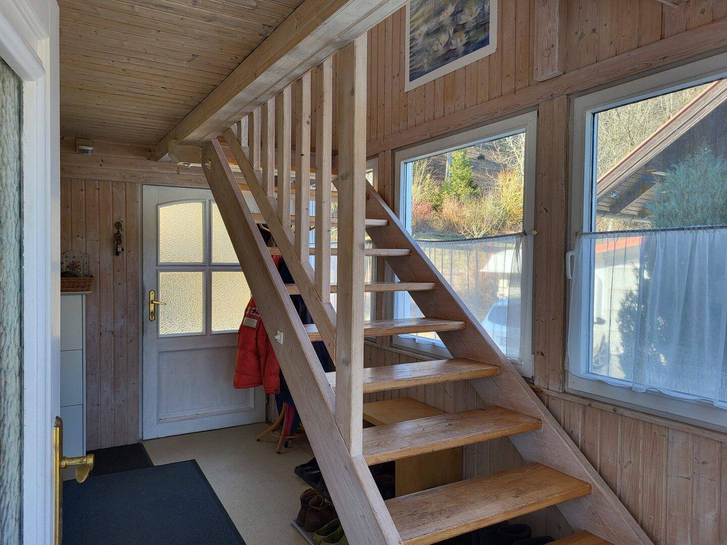 Eingangsbereich mit Holztreppe, Holzvertäfelung und einer Haustür, die zum Obergeschoss führt.