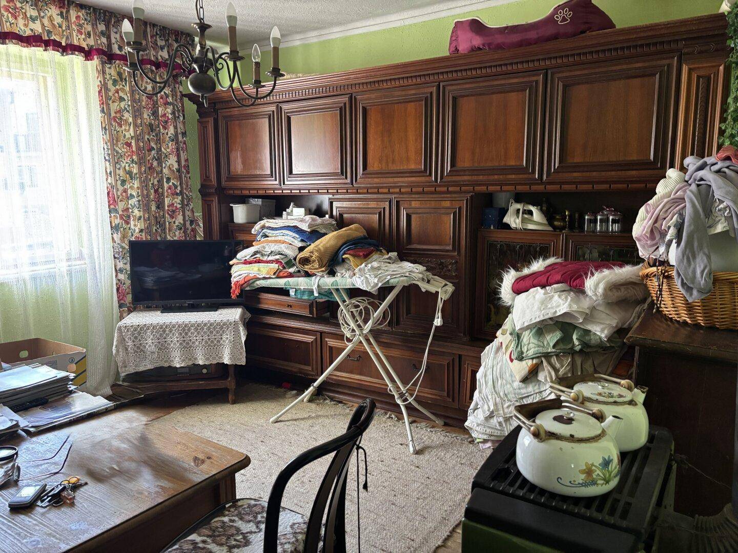 Wohnzimmer mit großem Holzschrank, Fernseher und traditionellen Vorhängen.