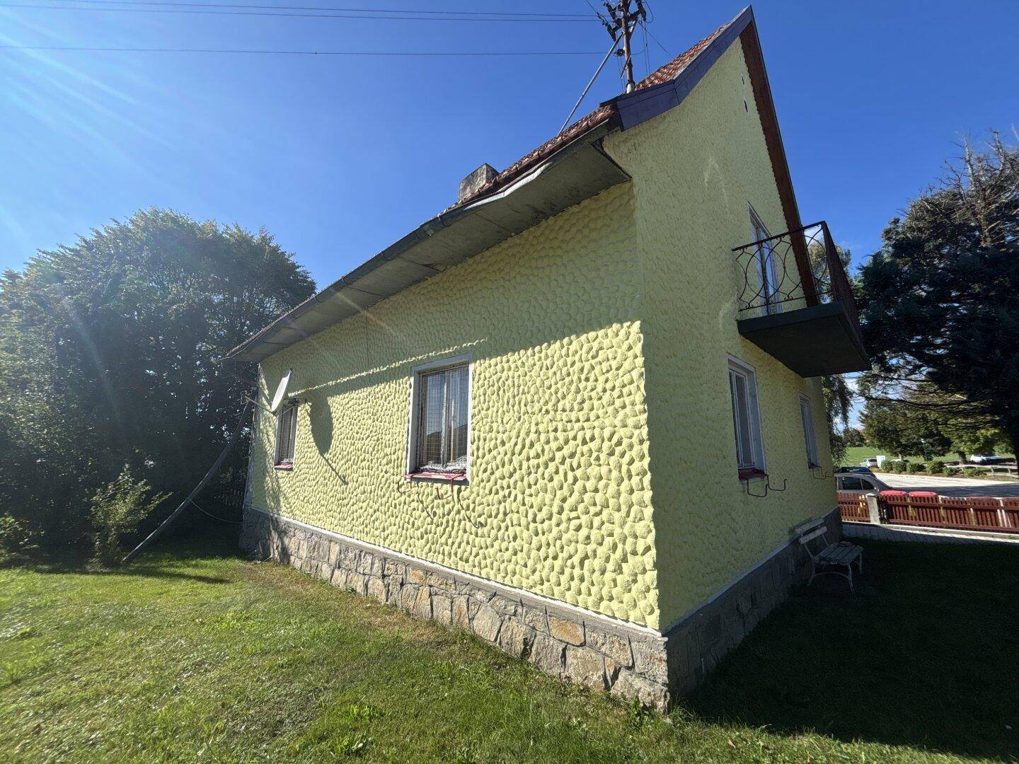 Seitenansicht des gelben Hauses mit strukturierter Fassade und kleinem Balkon.