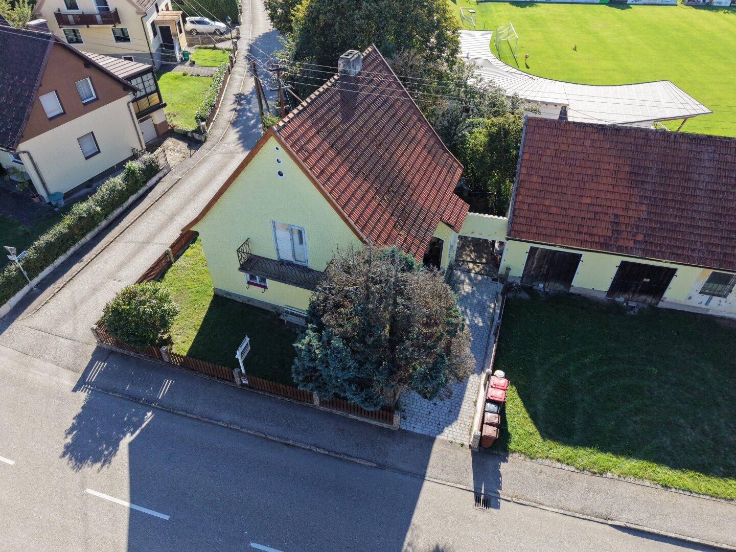 Vogelperspektive des gelben Hauses mit Hof, Nebengebäude und angrenzender Straße.