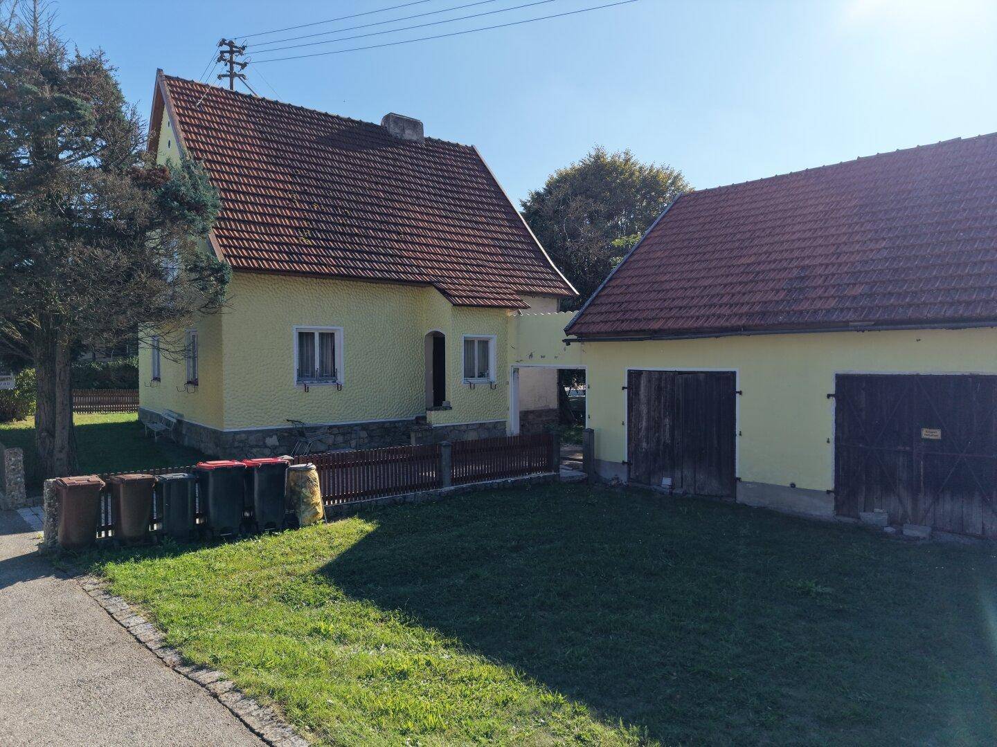 Gelbes Haus mit Nebengebäude und Gartenbereich unter blauem Himmel.